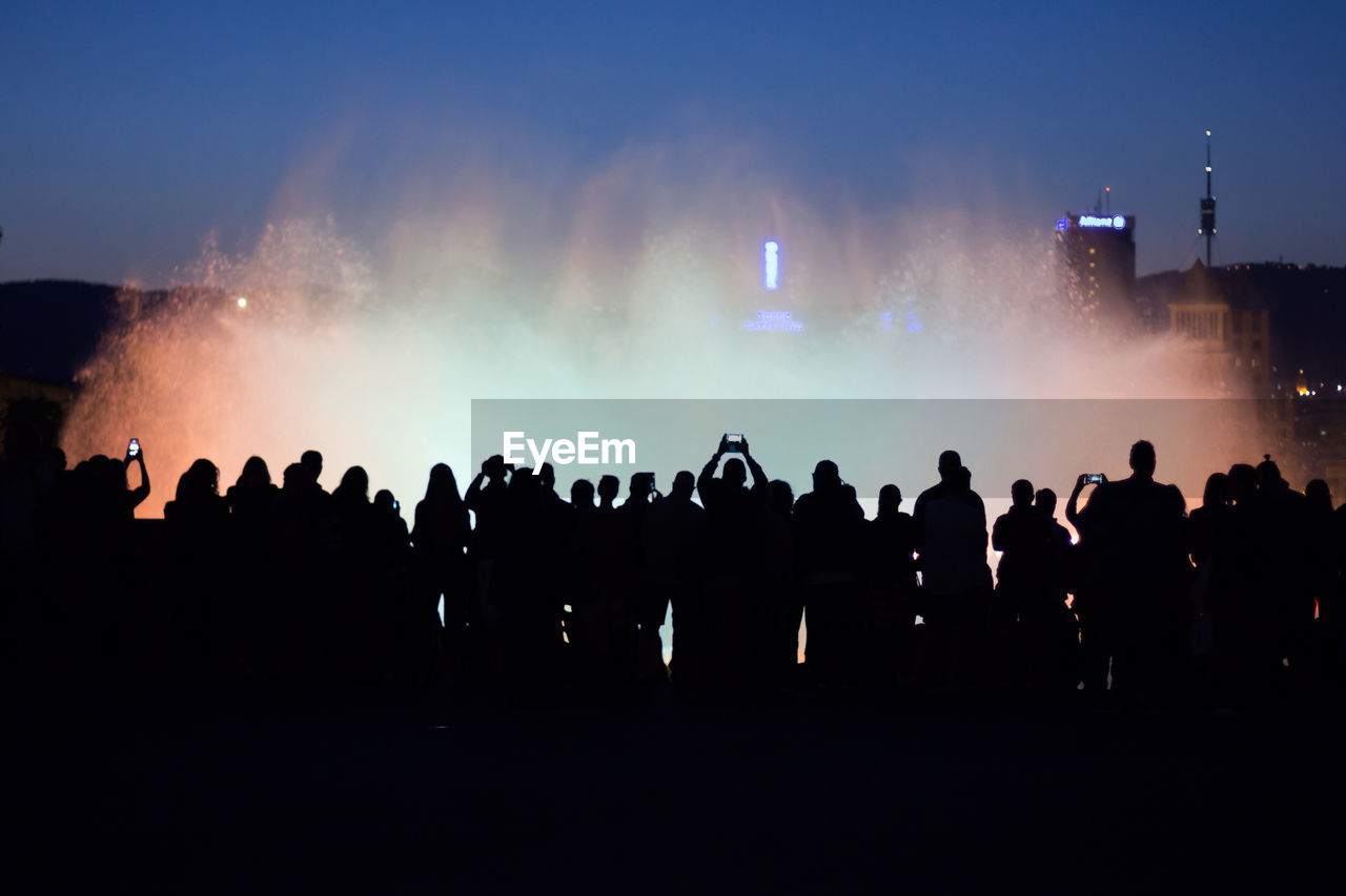 Silhouette people standing by fountain against sky at night