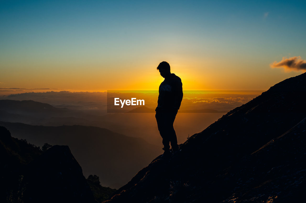 SILHOUETTE MAN STANDING AGAINST MOUNTAIN DURING SUNSET
