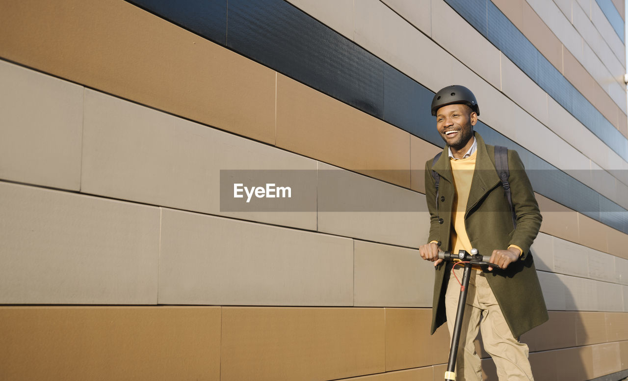 Happy man with helmet and scooter passing a building