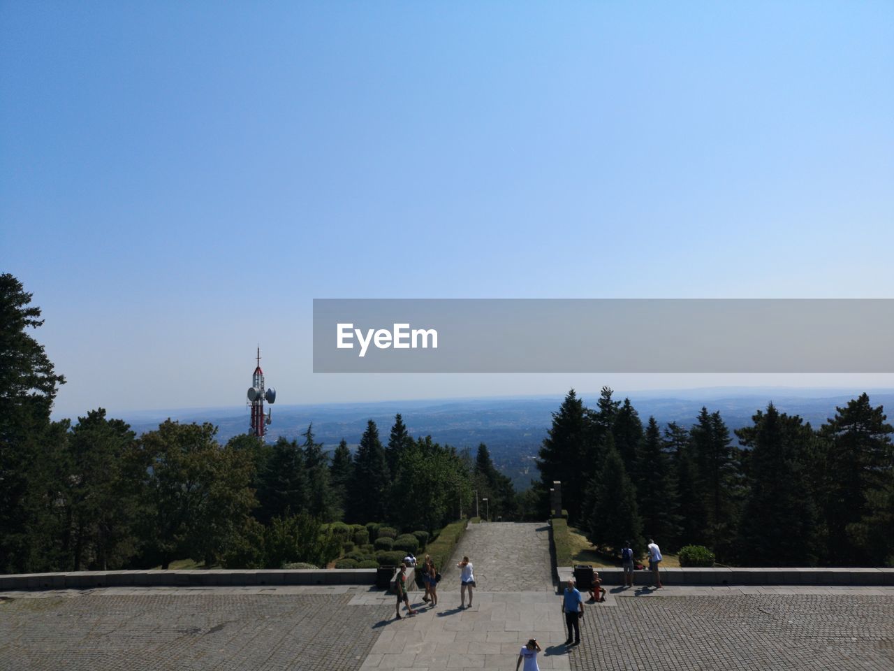 PEOPLE BY TREES AND BUILDINGS AGAINST CLEAR SKY