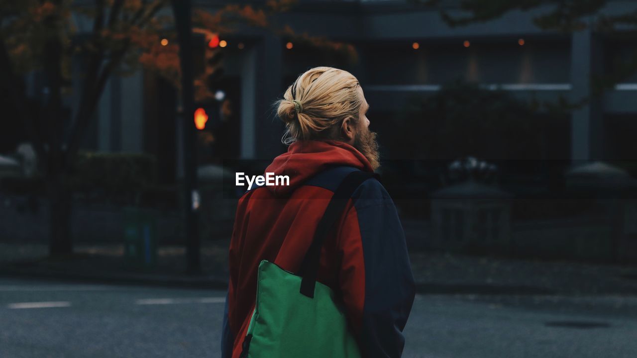 REAR VIEW OF WOMAN STANDING ON STREET AT CITY