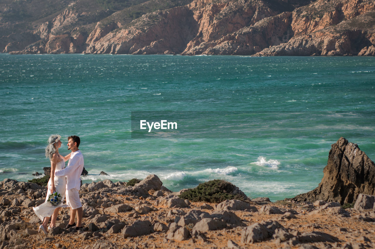 Full length of couple standing on rock by sea