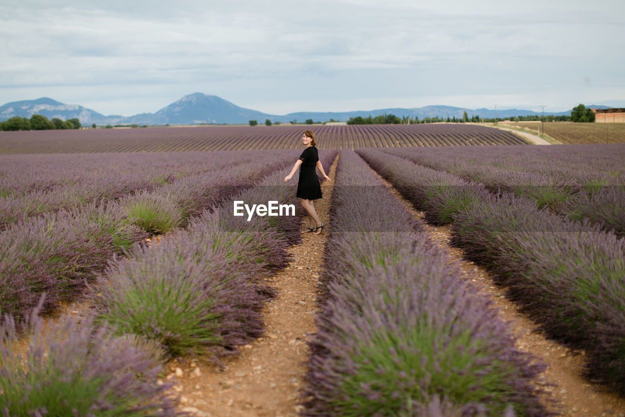 Full length of woman standing in lavender farm against sky
