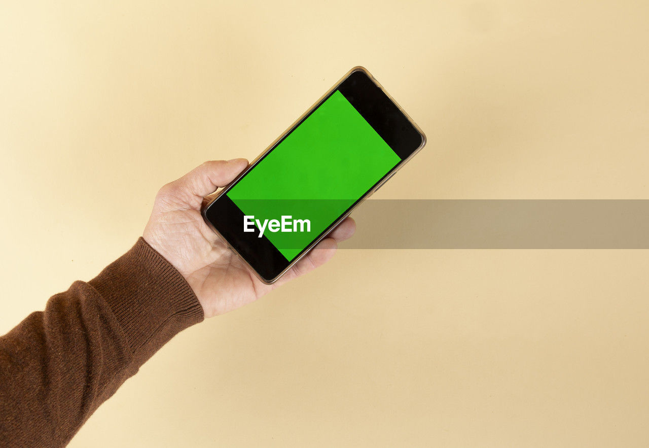 hand, technology, one person, holding, communication, green, wireless technology, studio shot, indoors, copy space, adult, close-up, yellow, portable information device, smartphone, screen