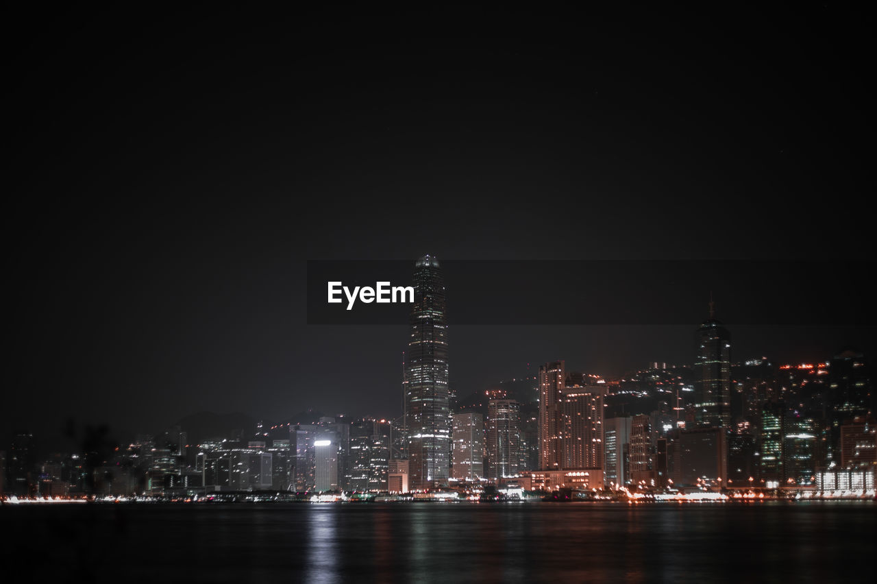 ILLUMINATED BUILDINGS BY RIVER AGAINST SKY AT NIGHT