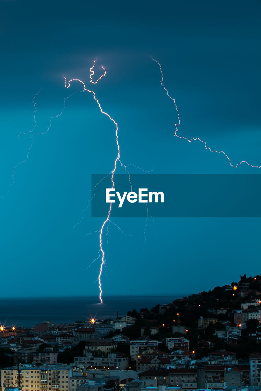 Lightning over sea by city at dusk