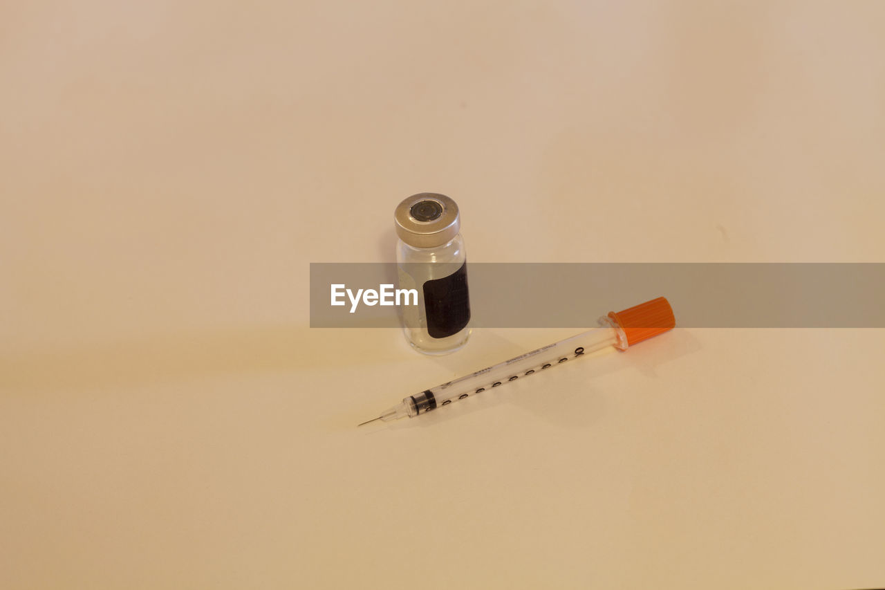 High angle view of syringe and medicine bottle on beige background