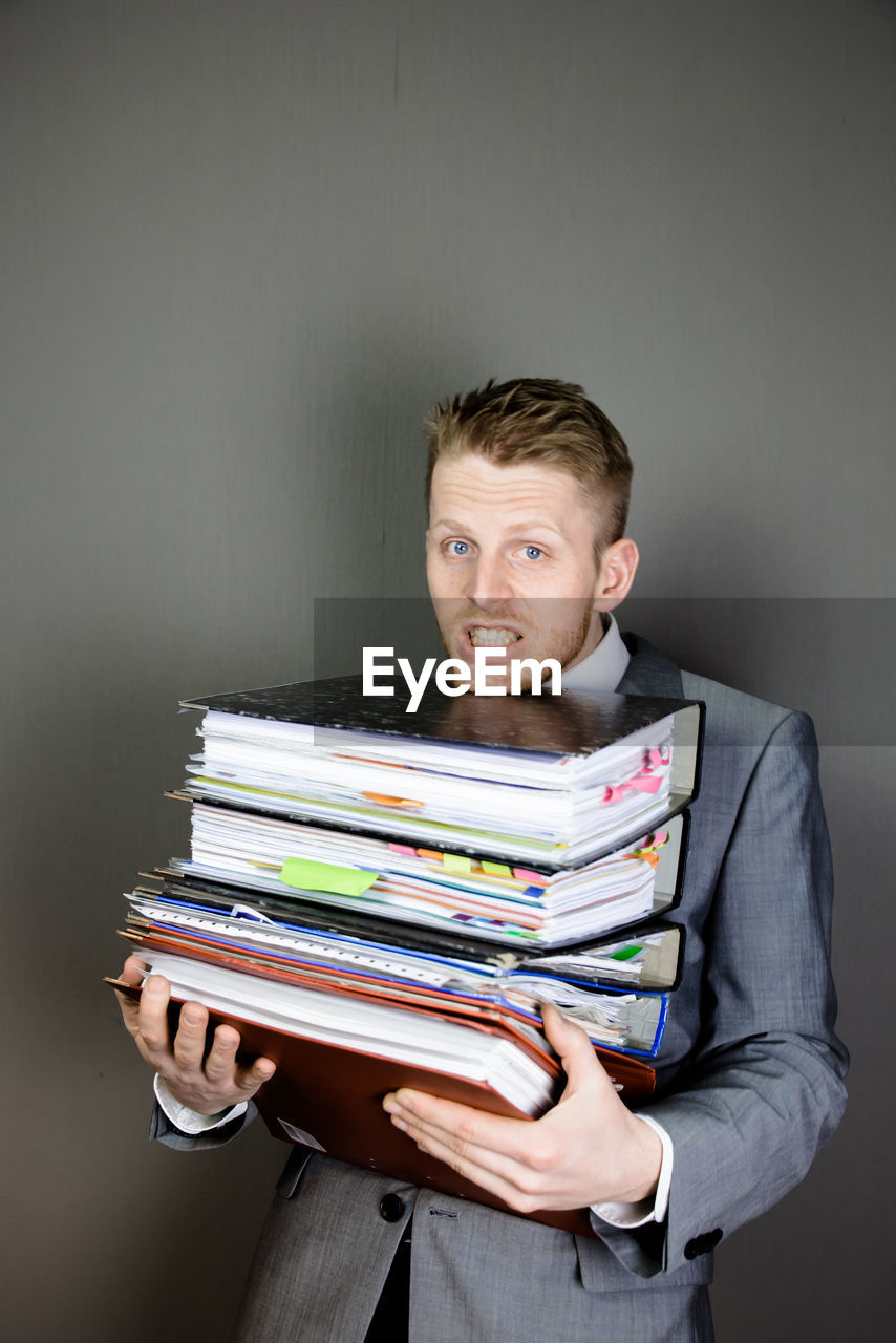 Tired businessman holding stacked files against gray background