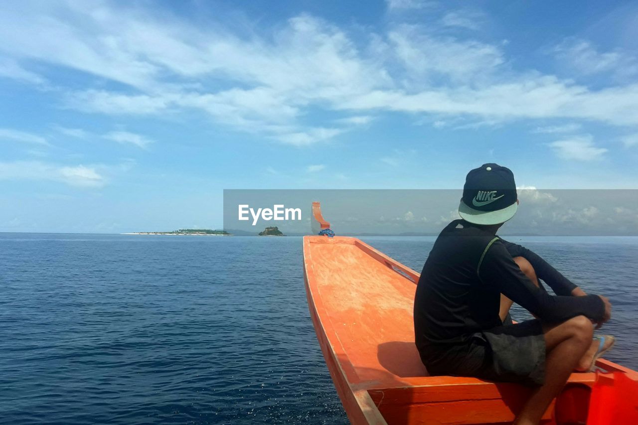 MAN SITTING ON SHORE AGAINST SKY