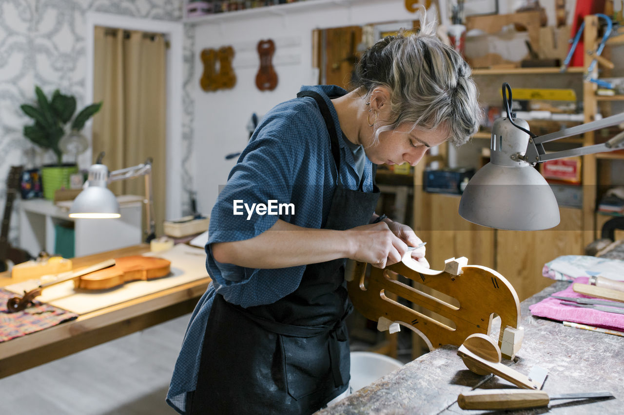 Luthier carving on violin at desk in workshop