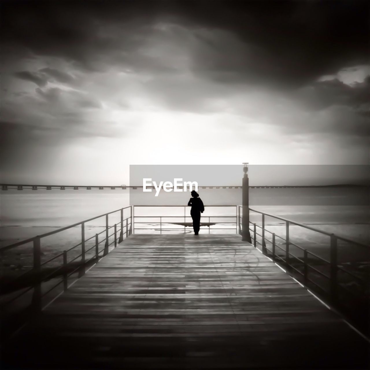 Silhouette woman on pier against cloudy sky at dusk