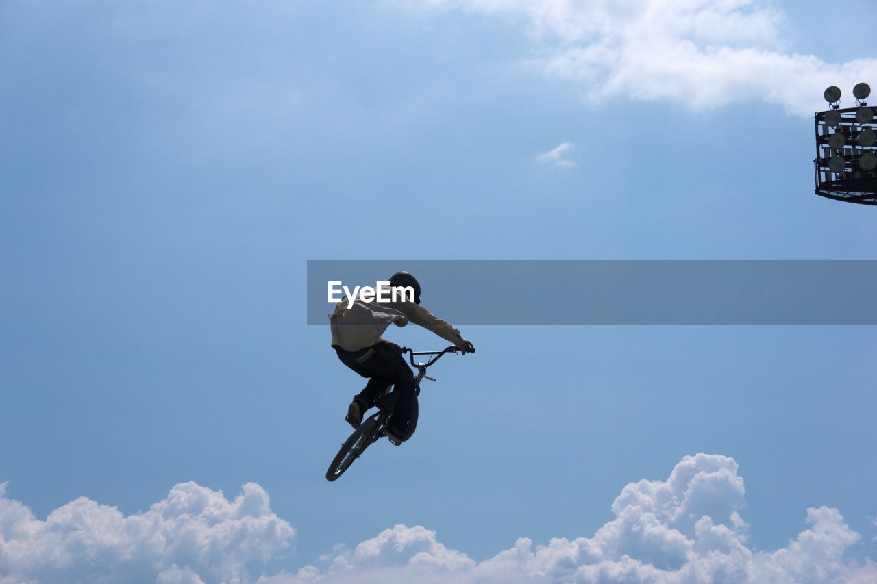 Low angle view of man with bicycle performing stunt against sky during sunny day