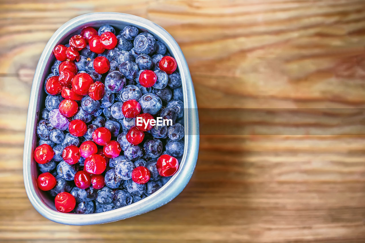 Frozen blueberries and cranberry in a gray cup on wooden background close-up. space for copy.