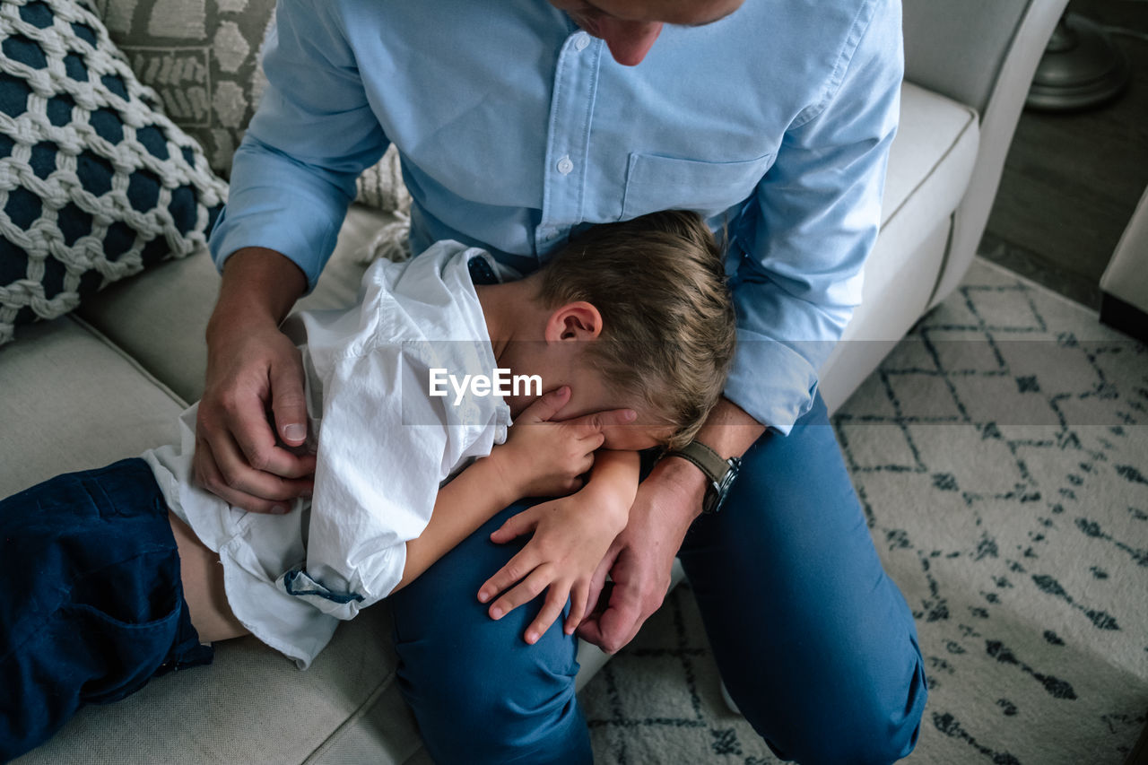 Young son hiding his face and laying on dad