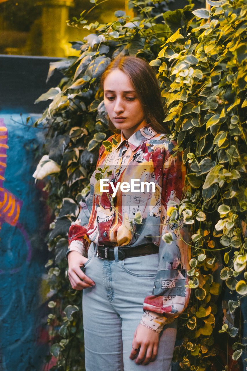 YOUNG WOMAN LOOKING DOWN WHILE STANDING IN AUTUMN