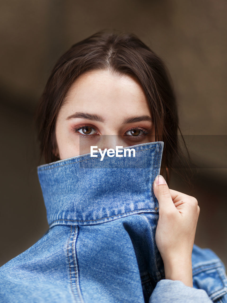 Girl with beautiful brown eyes covers her face with a denim collar