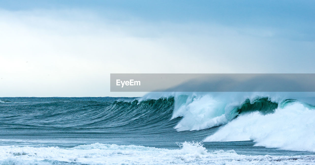 Sea waves splashing on shore against sky