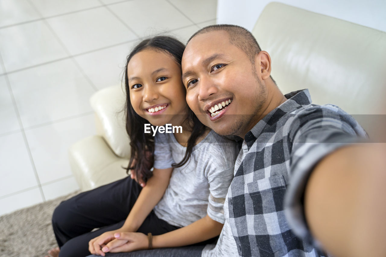 PORTRAIT OF HAPPY FRIENDS SITTING ON SOFA AT HOME