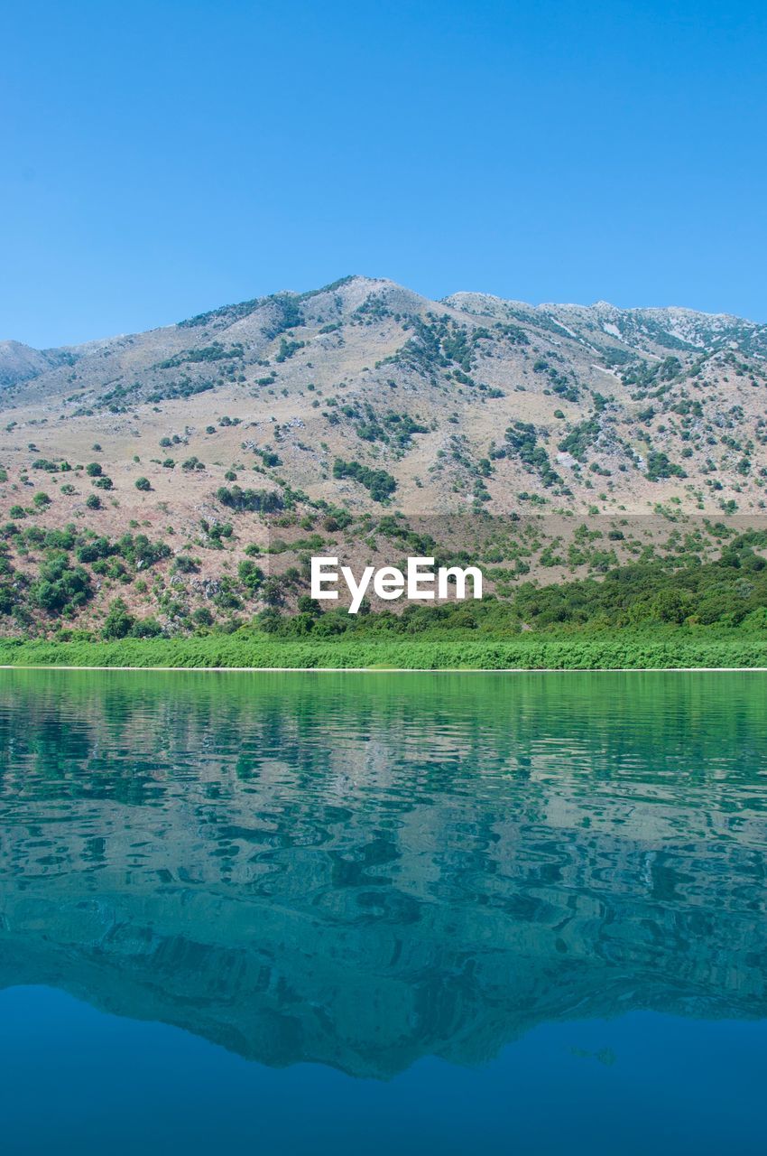 Scenic view of lake by mountains against clear blue sky