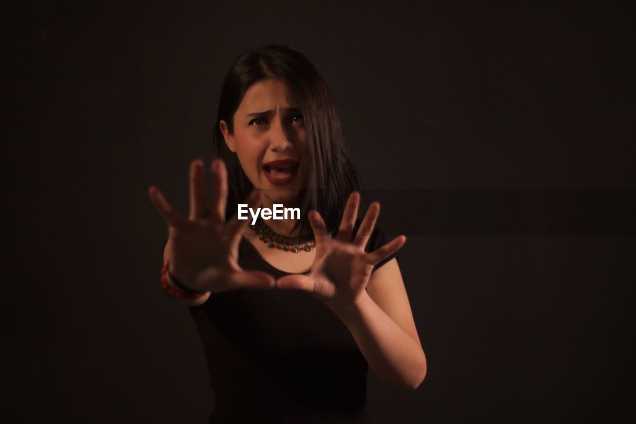 Scared woman gesturing while standing against black background