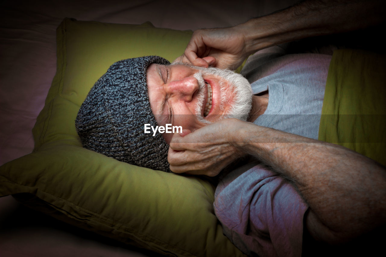 Senior man covering ears on bed at home