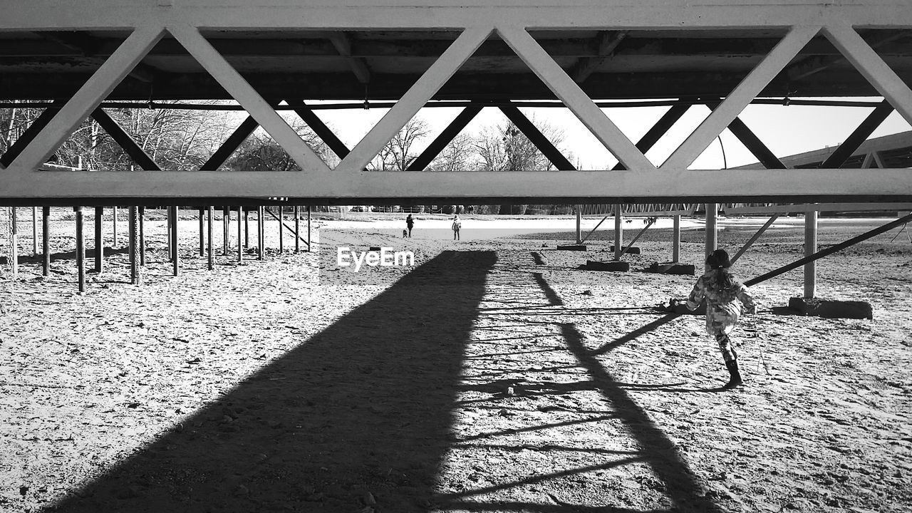 Rear view of girl running on sand at beach under pier