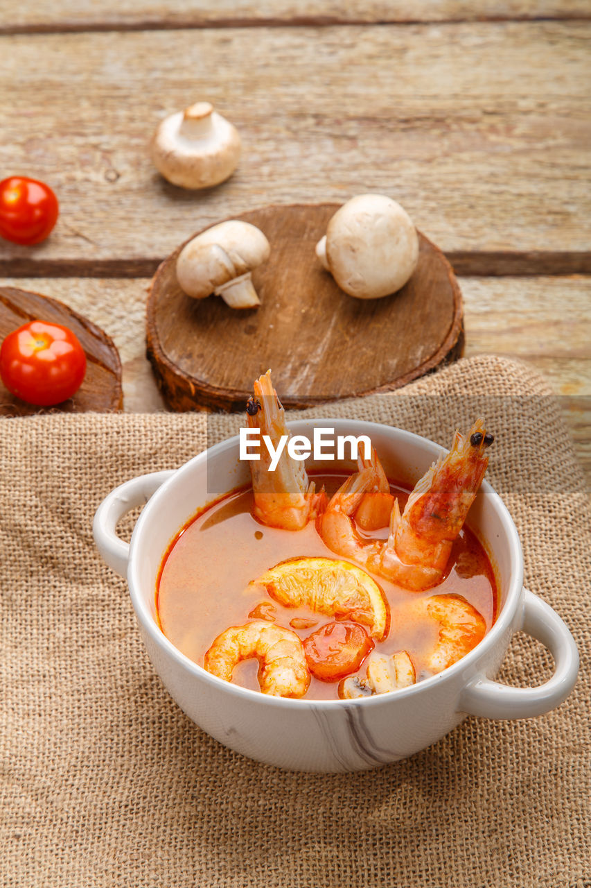 Tom yam soup with shrimps and coconut milk in a tureen vertical photo