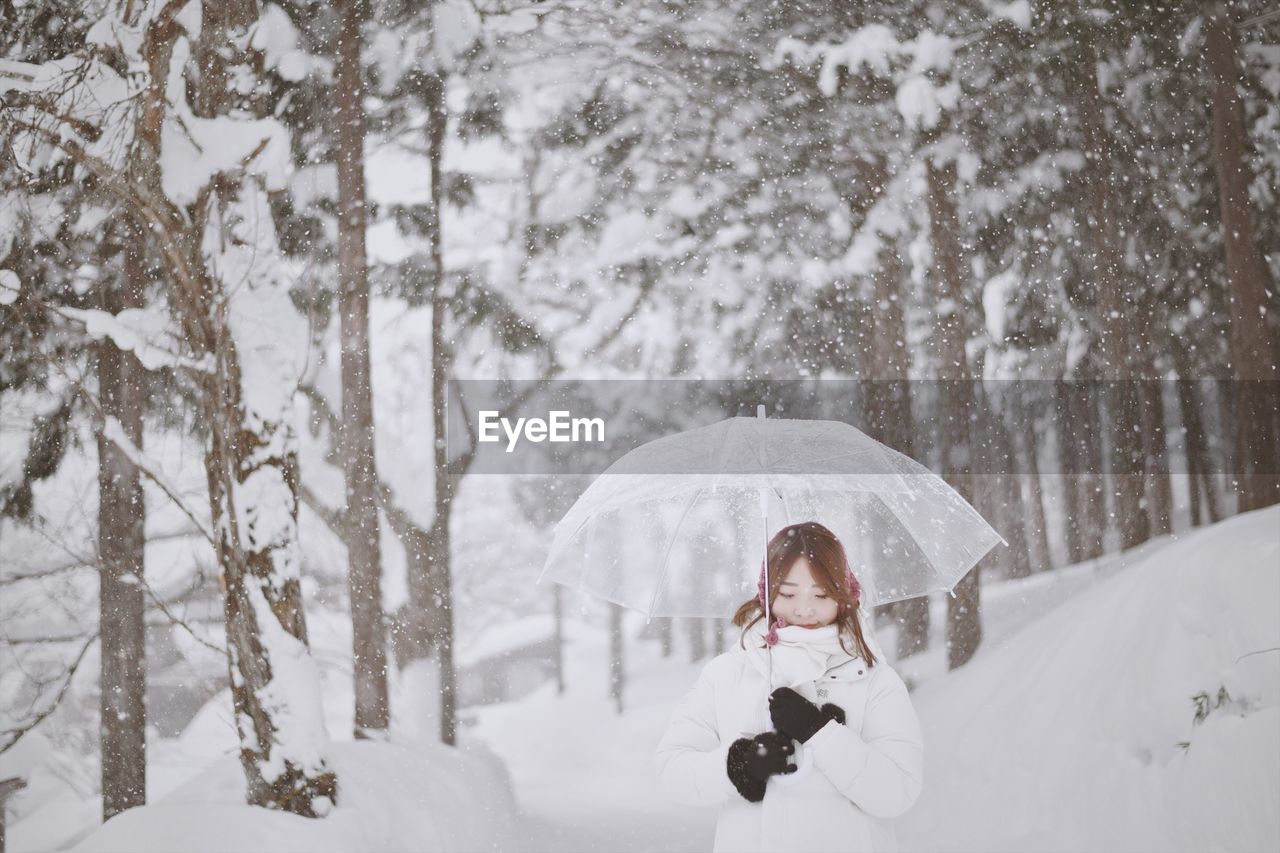 Woman with umbrella standing against trees during winter