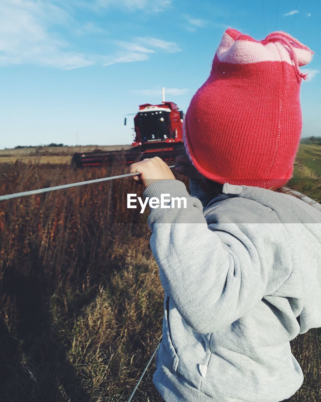 Close-up of kid wearing warm clothing while looking at combine harvester