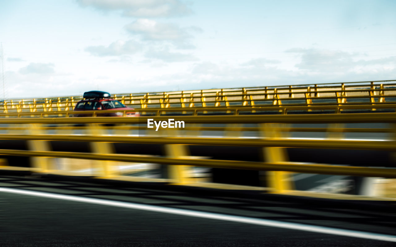 speed, transportation, blurred motion, motion, yellow, rail transportation, mode of transport, one person, real people, train - vehicle, bridge - man made structure, outdoors, public transportation, sky, architecture, day, people