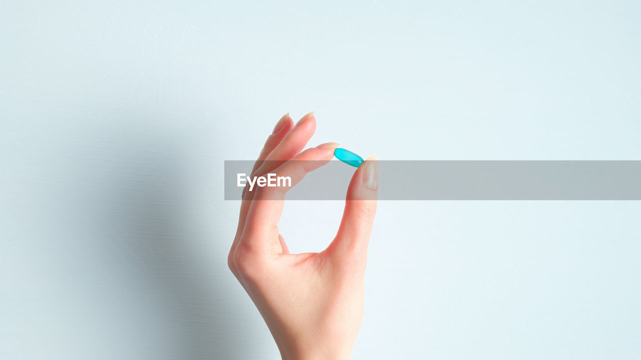 CLOSE-UP OF HAND HOLDING BLUE FLOWER AGAINST WHITE BACKGROUND