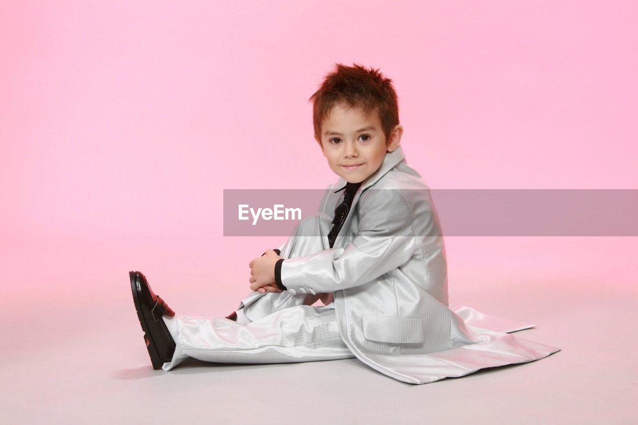 Portrait of boy sitting on pink background