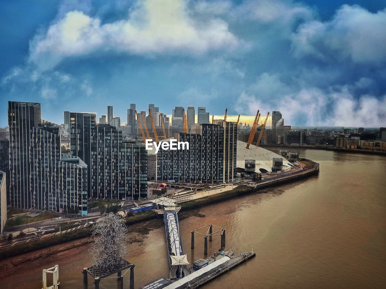 Modern buildings by river against sky in city