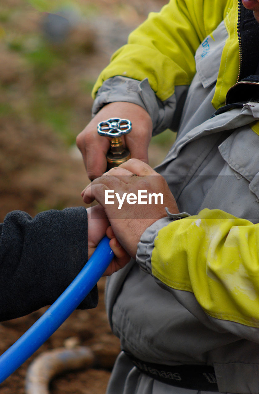 Cropped hand of person with worker holding pipe outdoors