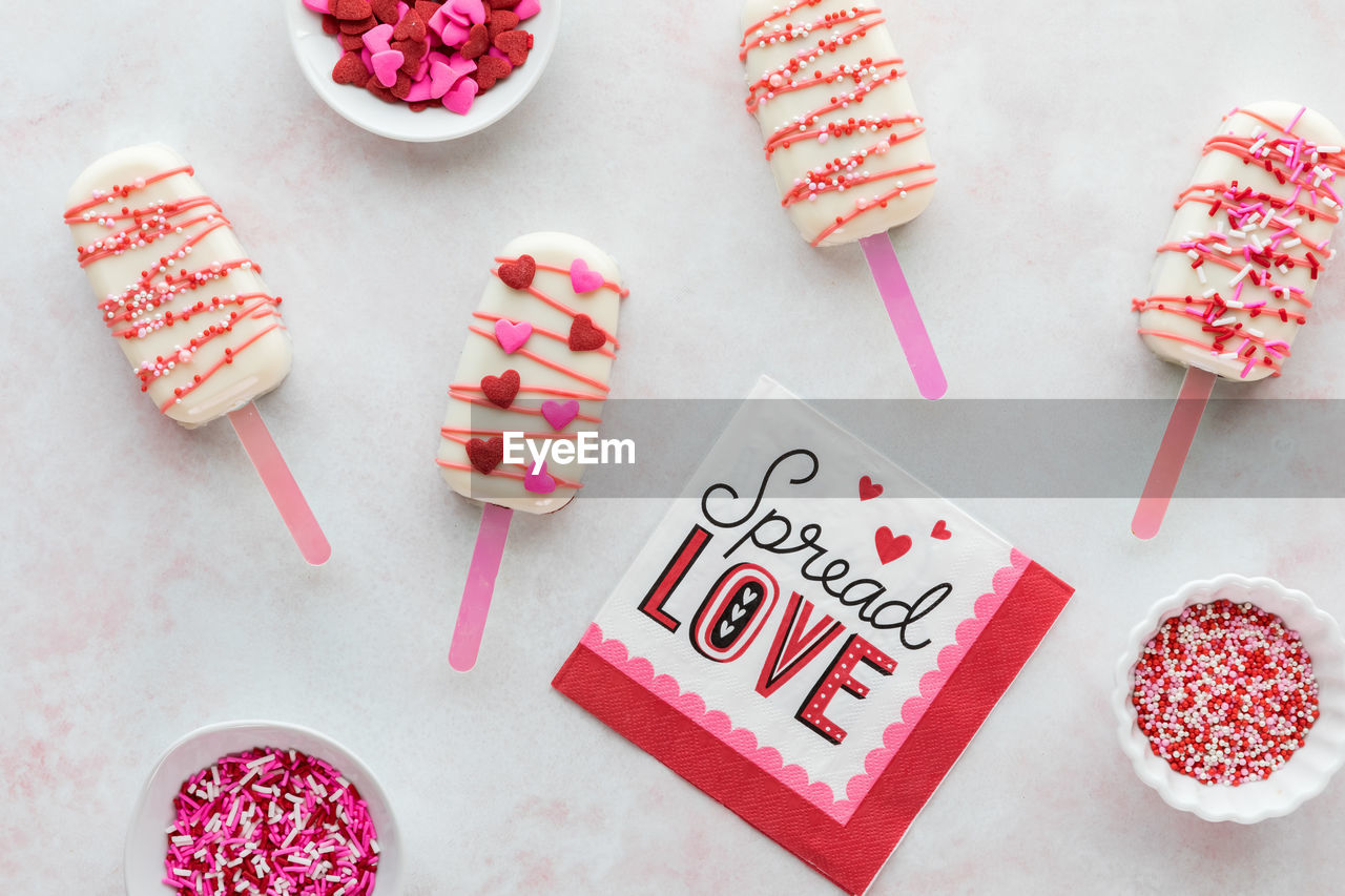 Homemade decorated cakesicles for valentine's day with bowls of sprinkles.