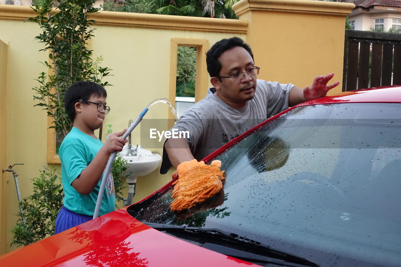 Boy assisting father while washing car