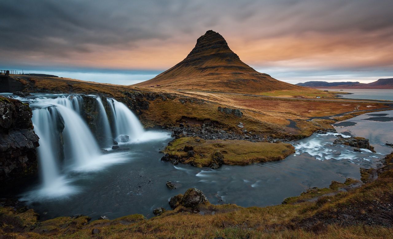 Scenic view of waterfalls and kirkjufell against cloudy sky at sunset