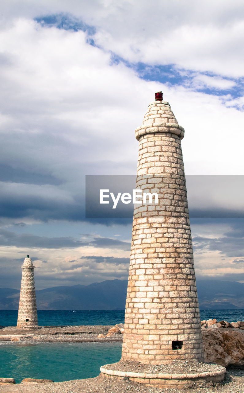 Lighthouse at seashore against cloudy sky