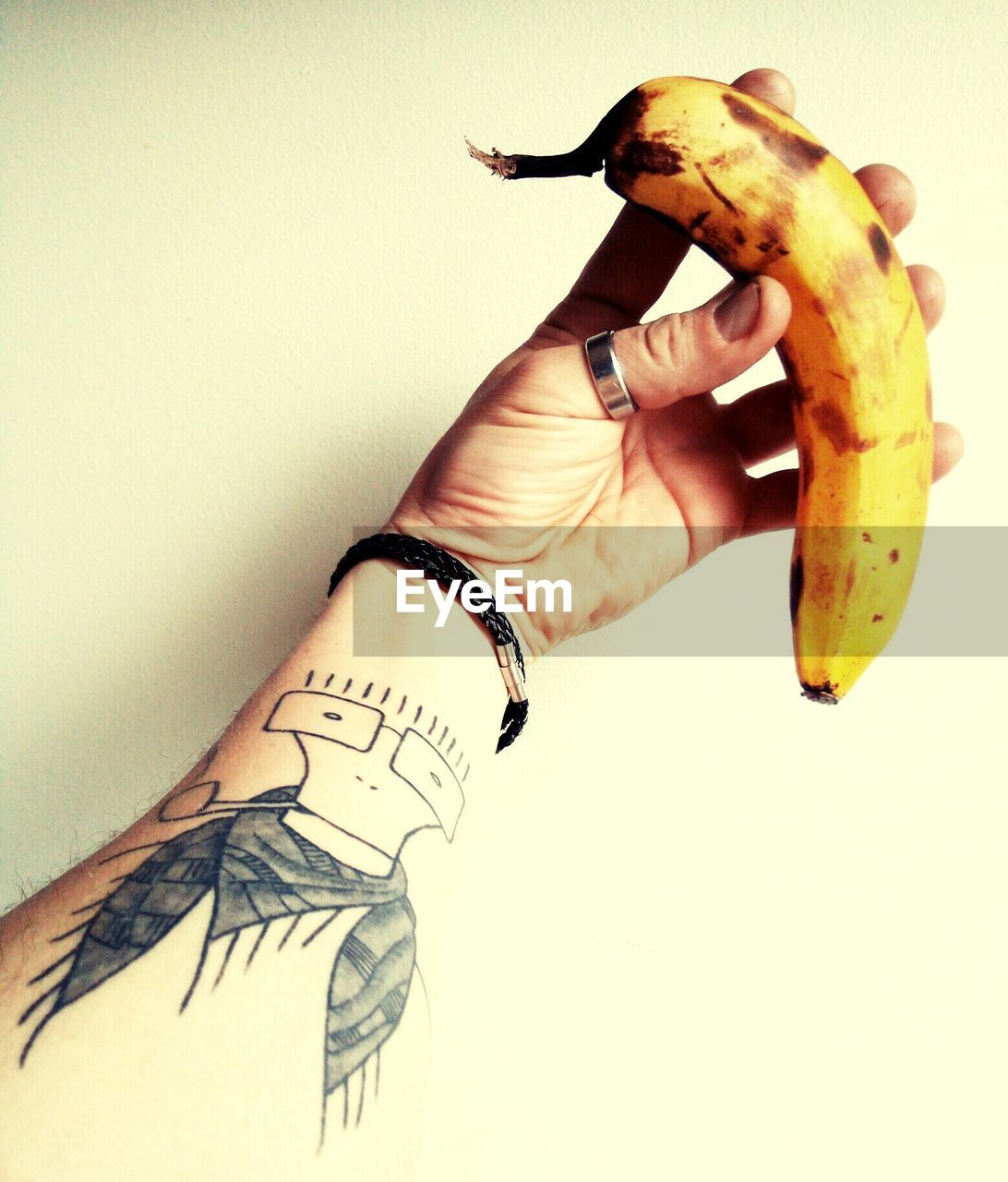 Tattooed hand holding banana against wall