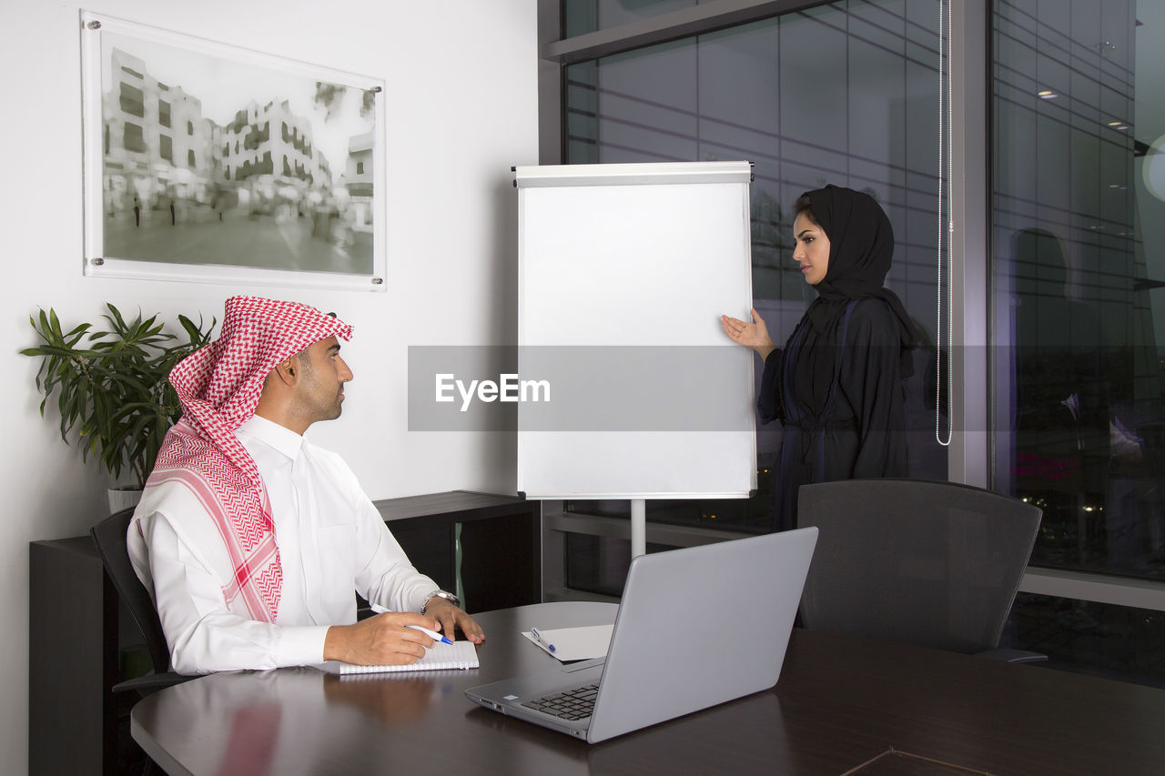 Woman standing by whiteboard looking at man in office