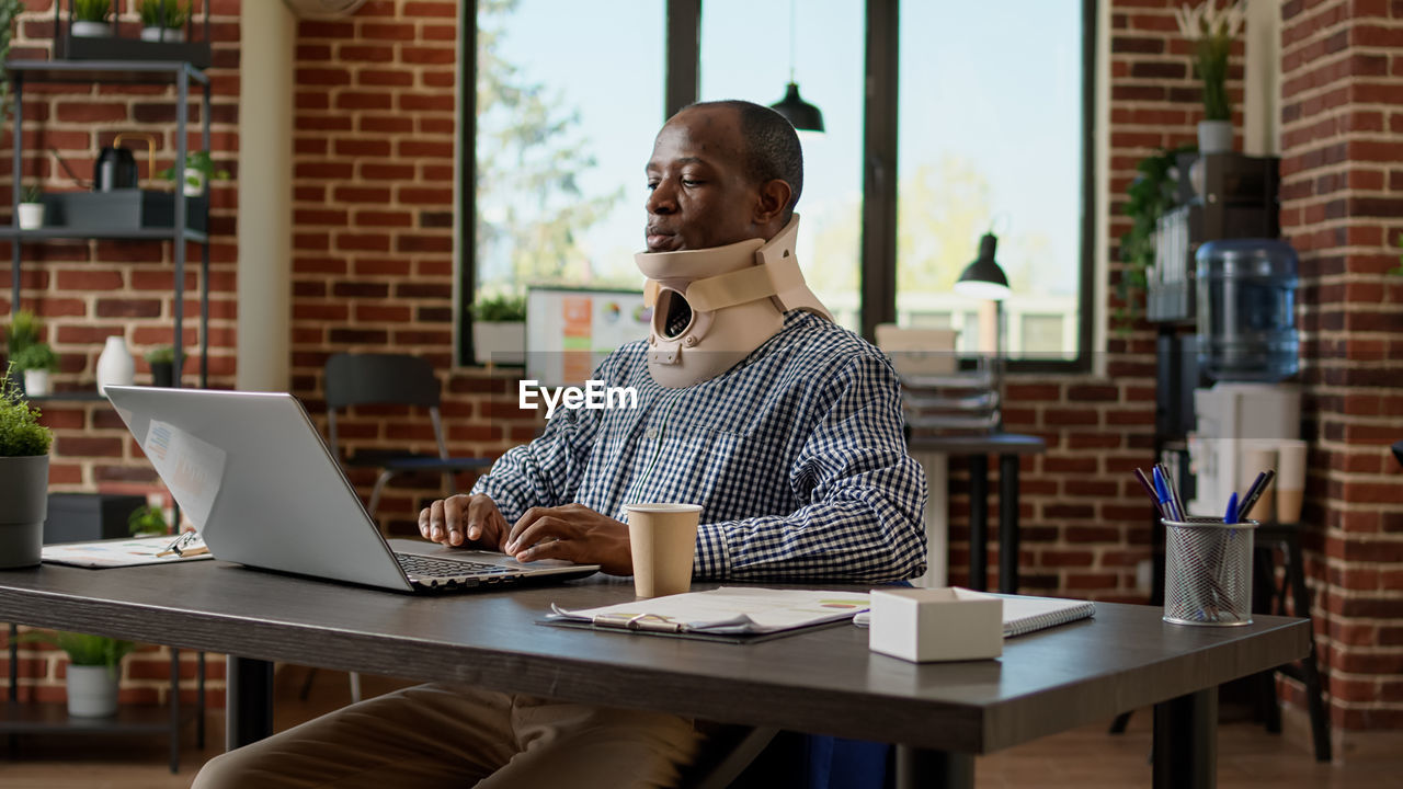 Businessman with neck brass using laptop in office