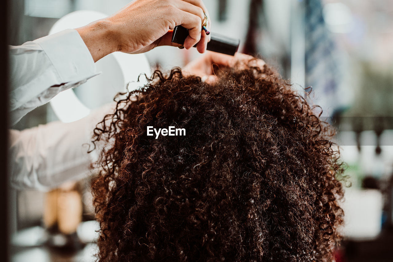 Cropped hands of barber combing woman hair in salon