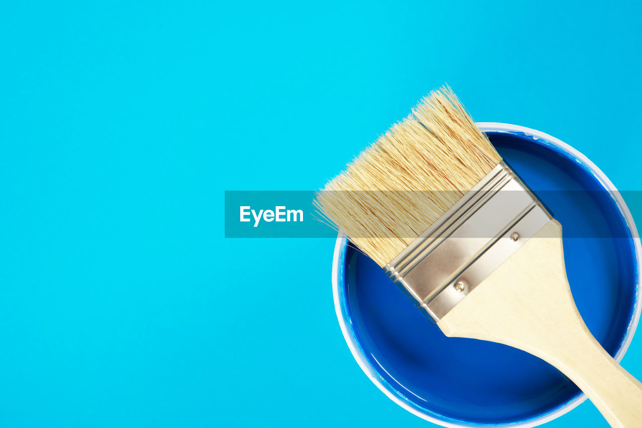 A paint brush is placed on a paint can. with blue background