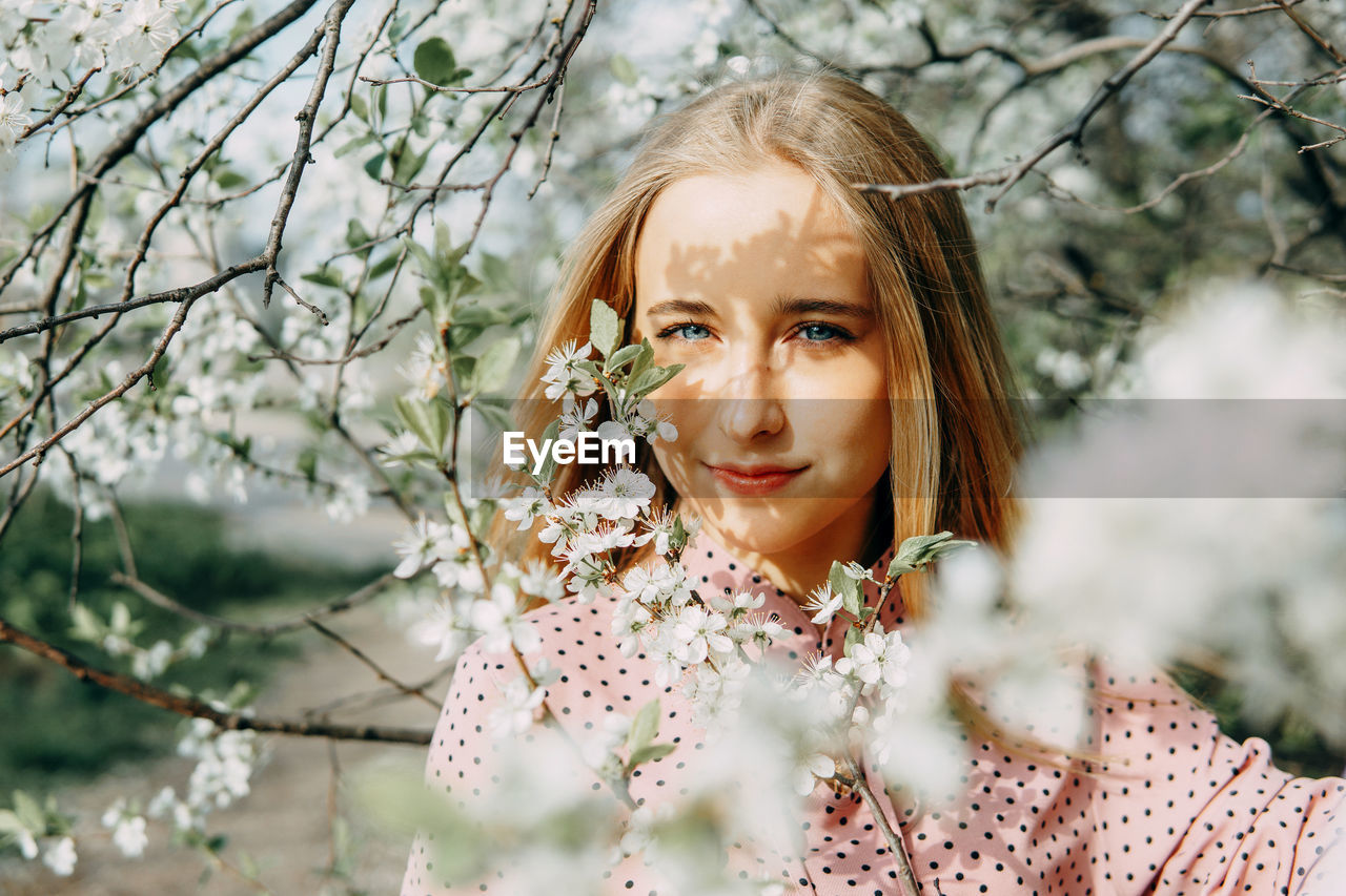 Blonde girl on a spring walk in the garden with cherry blossoms. female portrait, close-up. 