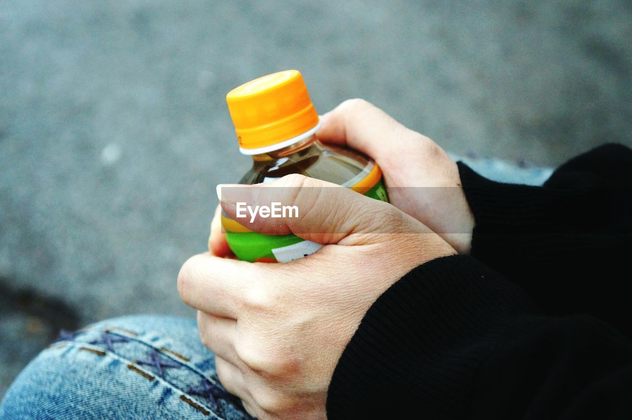 Cropped image of hands holding bottle while sitting outdoors