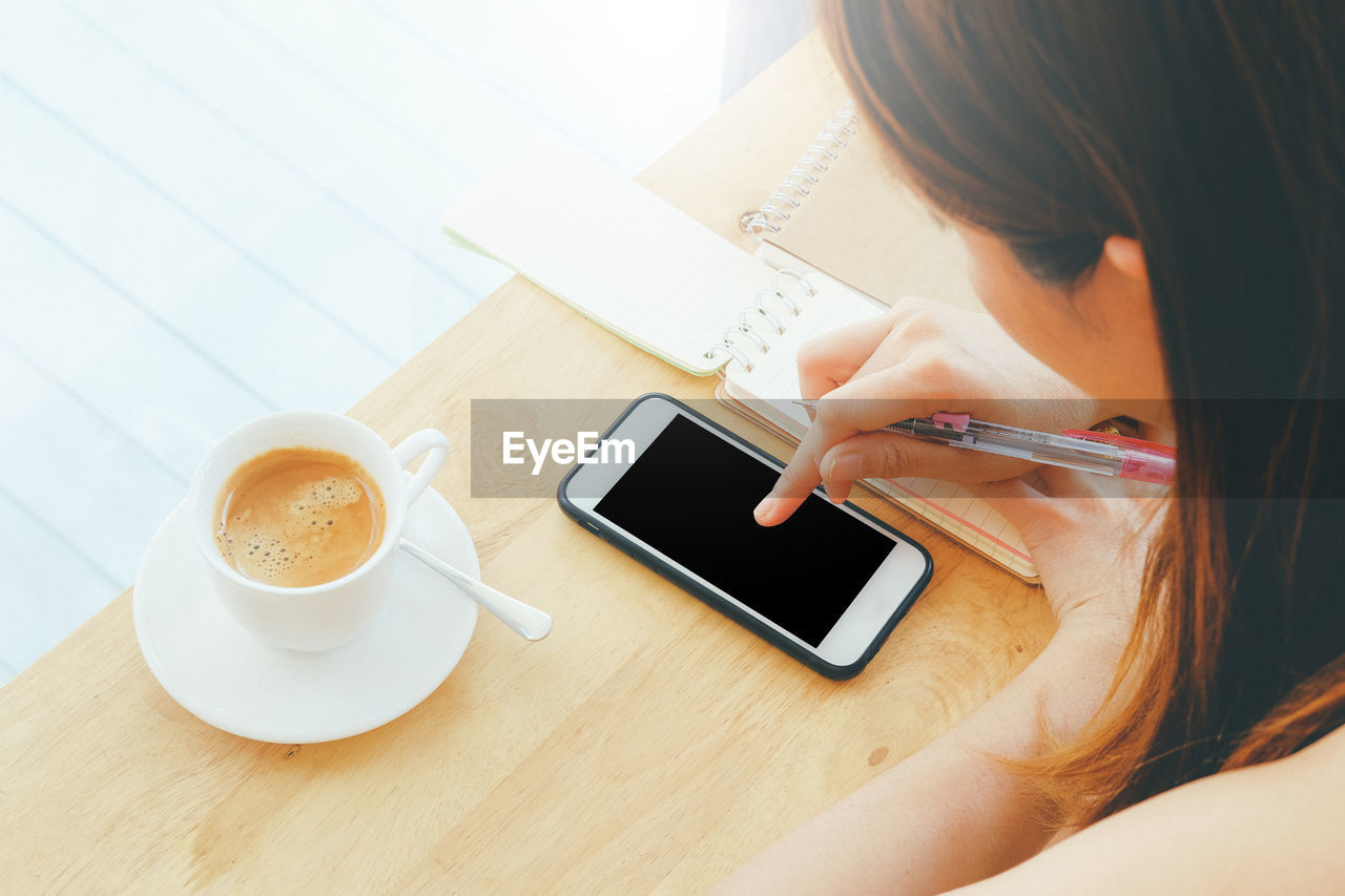 High angle view of woman using phone while having coffee at table