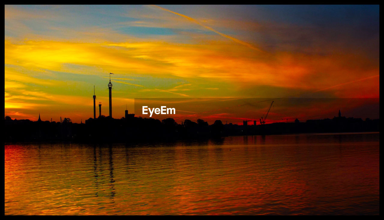 Scenic view of lake by silhouette buildings against sky during sunset