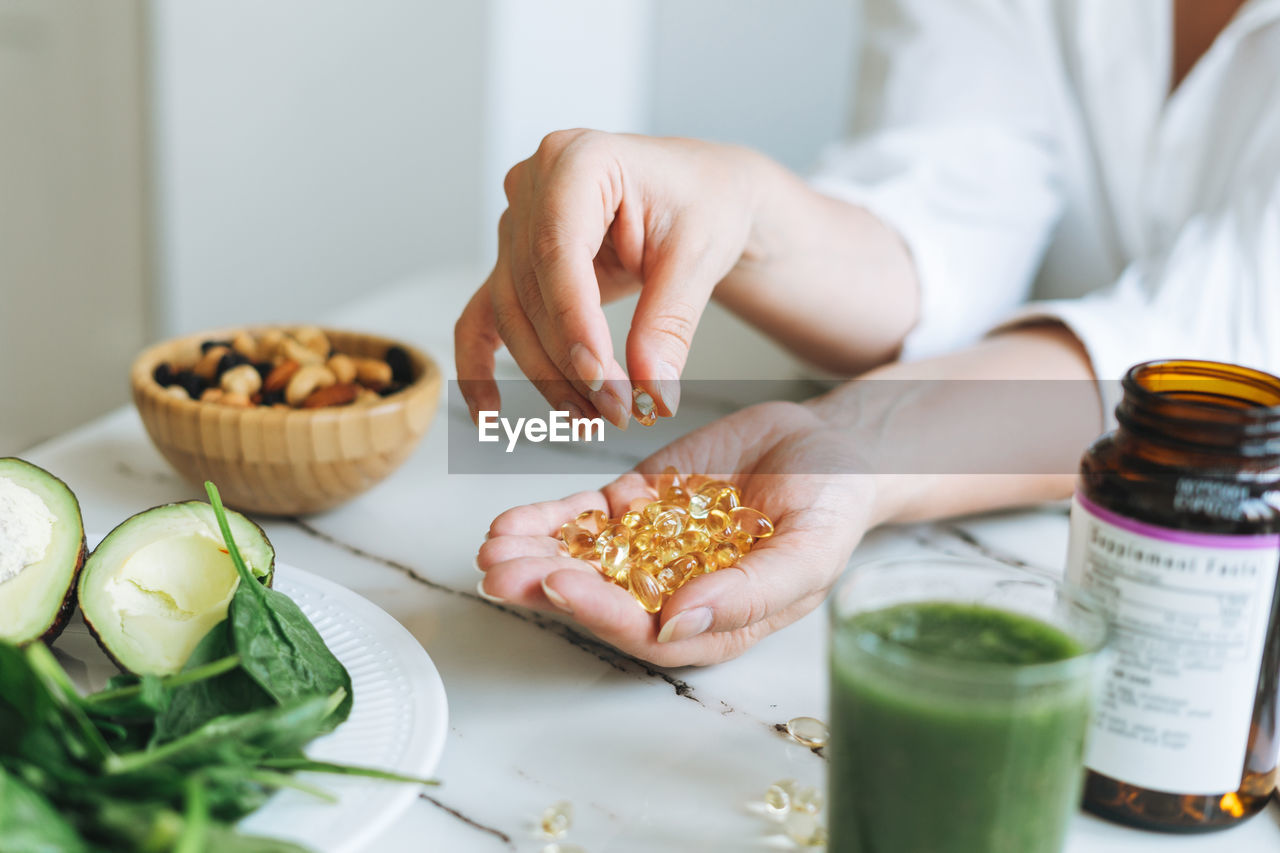 Woman doctor nutritionist hands in white with omega 3, vitamin d capsules with green vegan food