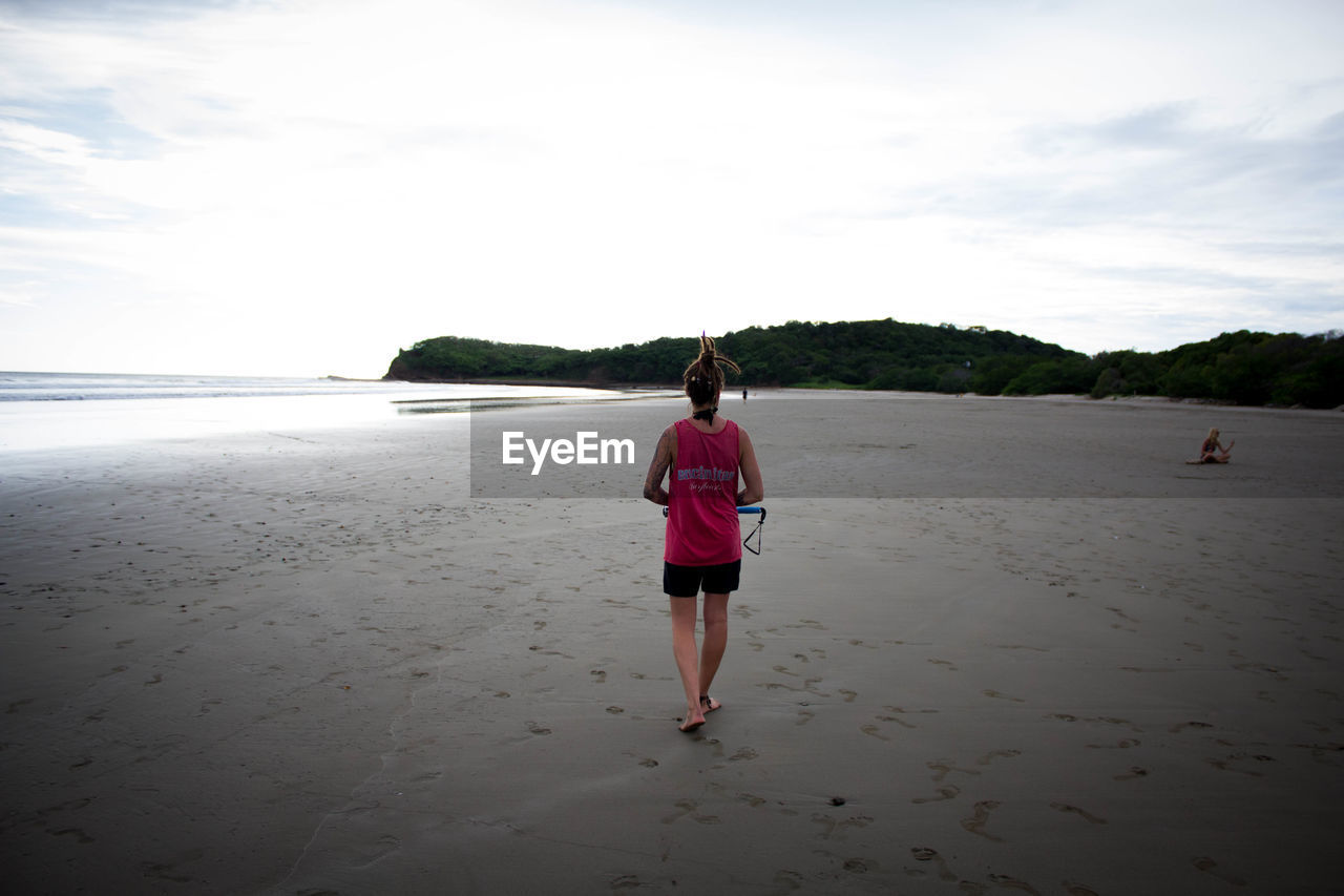 REAR VIEW OF WOMAN STANDING ON BEACH