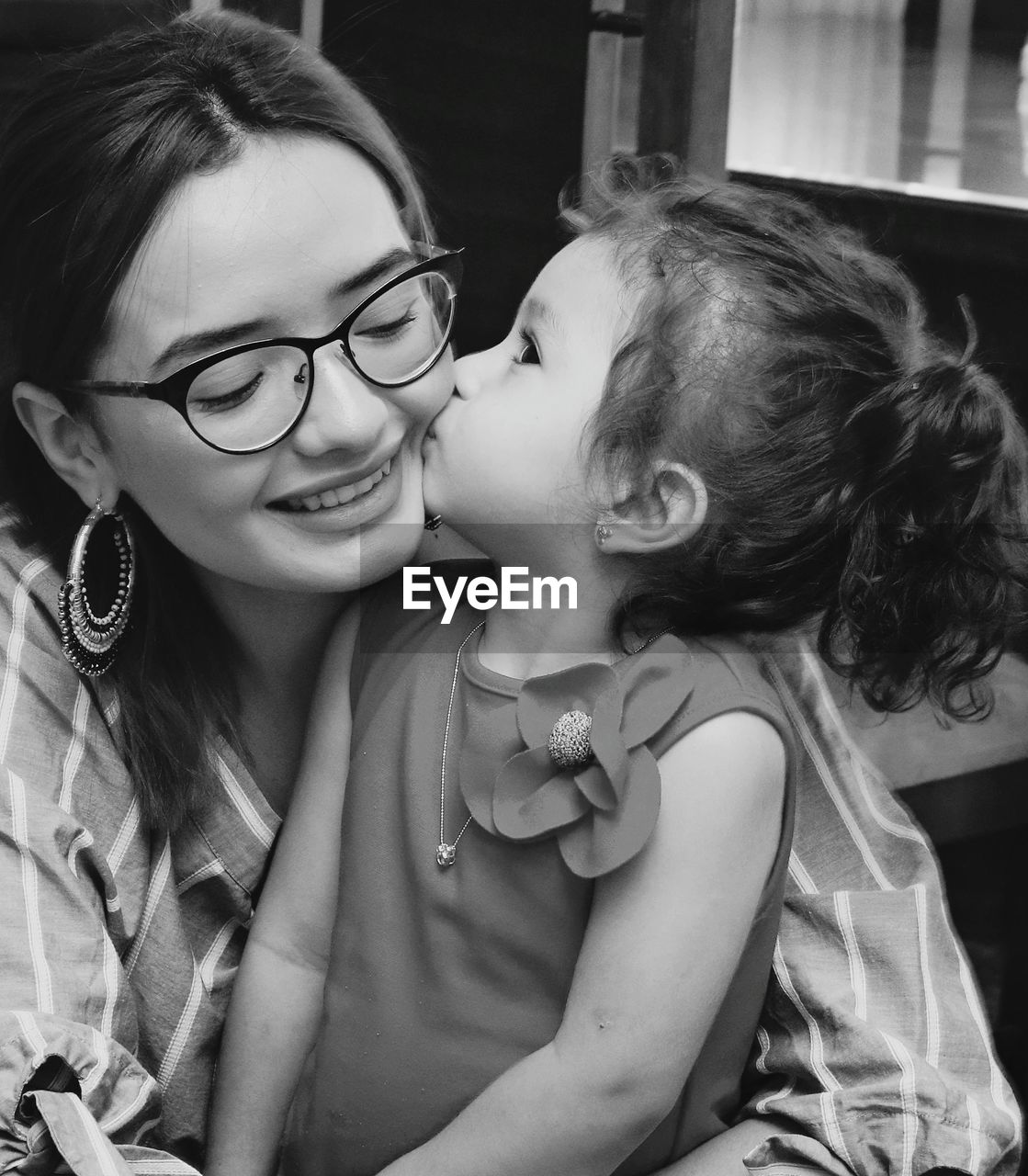 Close-up of cute daughter kissing happy mother at home